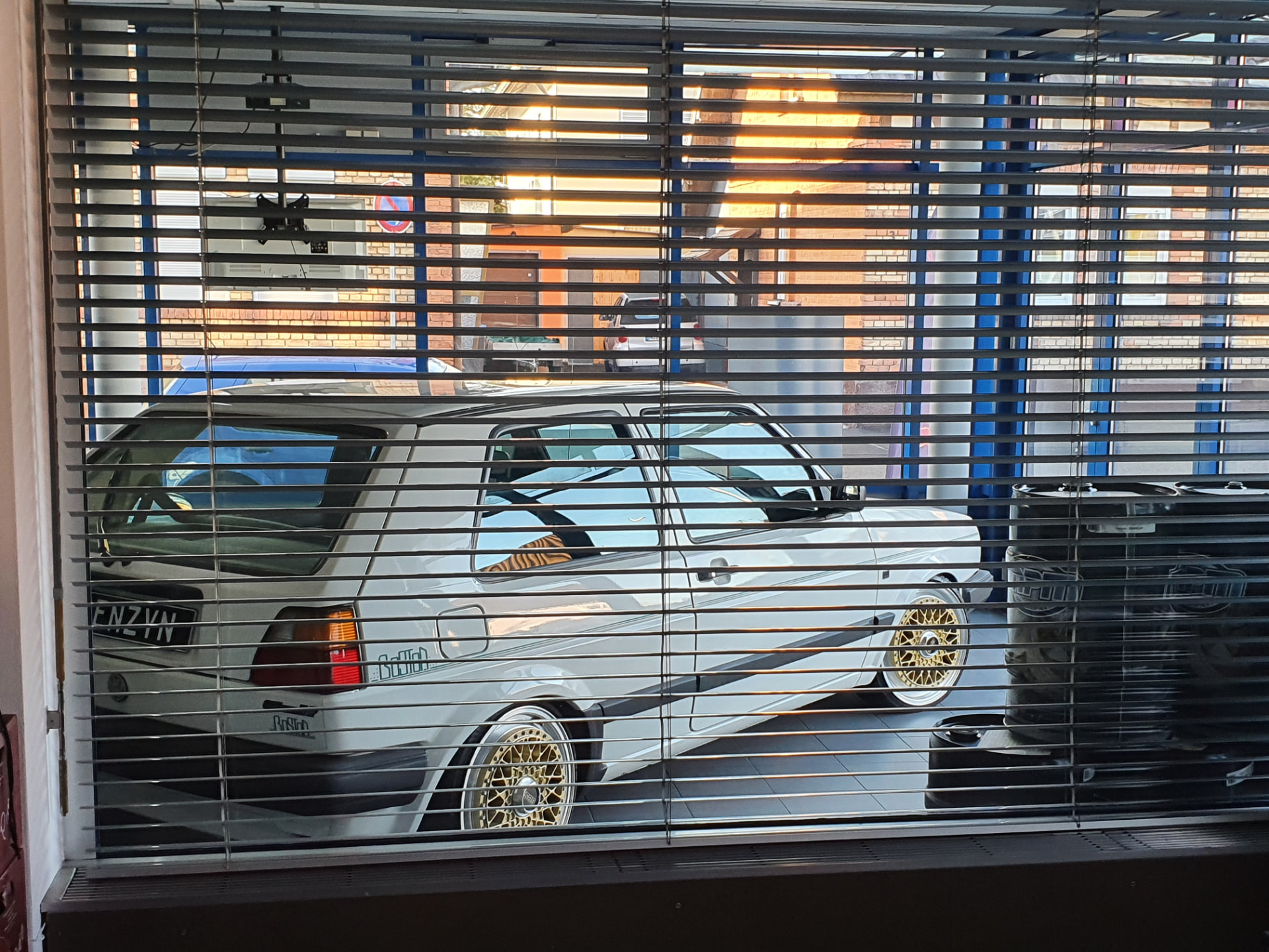VW Golf mit BENZYN-Kennzeichen vor der Werkstatt, Blick durch die Jalousie
